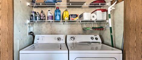 Une buanderie équipée de deux machines à laver à chargement frontal, d’étagères contenant des produits de nettoyage et d’un sèche-linge.