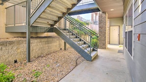 Un escalier extérieur abrité, menant à l’entrée d’un bâtiment, avec un mur en briques et un sol recouvert de gravier.