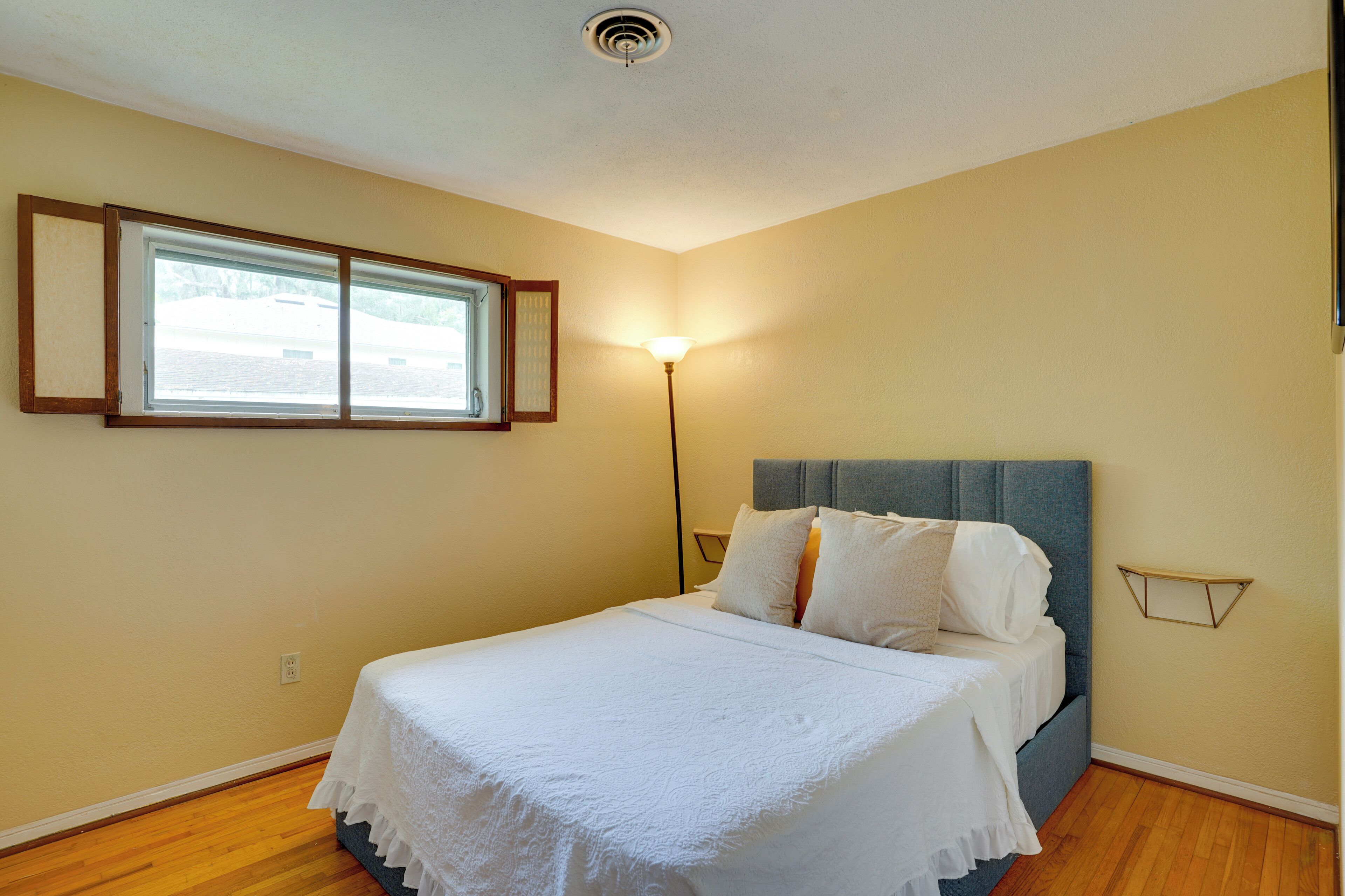 A bedroom with a bed, a window, a wall-mounted light, and a ceiling vent.