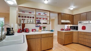 A modern kitchen with wooden cabinets, a white countertop, and various appliances including a microwave, oven, and coffee maker. - Charming Mid-century House - Just Steps to Lake! (Lakeland)
