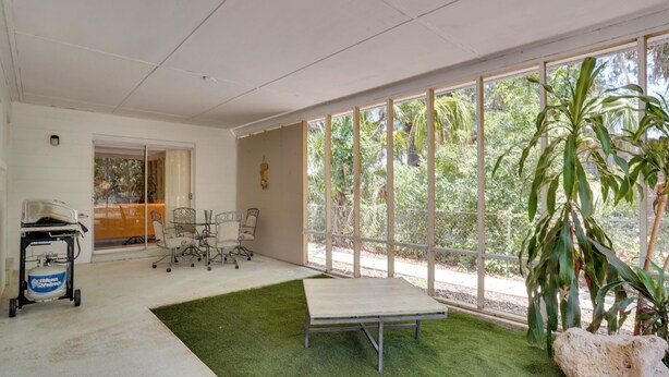 A spacious room with large windows, a green artificial turf area, a metal table, and a cart with a gas cylinder. - Charming Mid-century House - Just Steps to Lake! (Lakeland)