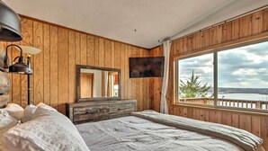 A bedroom with a large bed, wooden walls, a TV, and a view of a lake. - Lakeside Urbana Home - Near Hunting & Fishing! (Urbana)