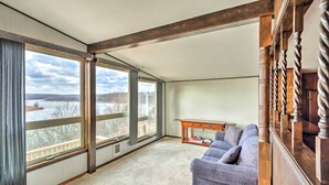 A spacious room with large windows offering a view of a lake and hills, a wooden ceiling, and a blue upholstered sofa. - Lakeside Urbana Home - Near Hunting & Fishing! (Urbana)
