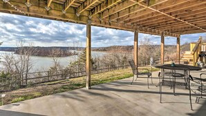 A covered outdoor area with a concrete floor, metal chairs, a table, and a view of a lake and trees. - Lakeside Urbana Home - Near Hunting & Fishing! (Urbana)