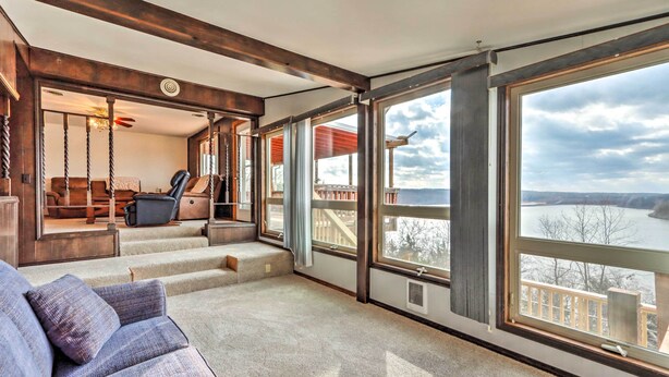 A spacious room with large windows offering a view of a body of water and a deck area with outdoor furniture. - Lakeside Urbana Home - Near Hunting & Fishing! (Urbana)