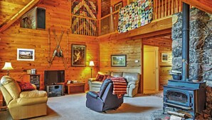 A cozy log cabin interior with a stone fireplace, a comfortable seating area, and a balcony with quilts. - Hot Tub, Deck & Trail Access: Shaver Lake Cabin (Shaver Lake)