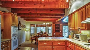 A wooden kitchen with a central island, built-in appliances, and a dining area with a table and chairs. - Hot Tub, Deck & Trail Access: Shaver Lake Cabin (Shaver Lake)