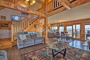 A spacious living area with a wooden staircase, a gray sofa, a glass coffee table, and a large window offering a view of the outdoors. - Mtn Views & Fire Pit: Rustic Piney Creek Cabin (Piney Creek)