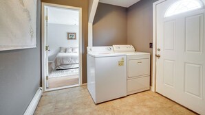 Un lavadero con lavadora y secadora, una puerta que da a un dormitorio, y una puerta blanca con ventana.