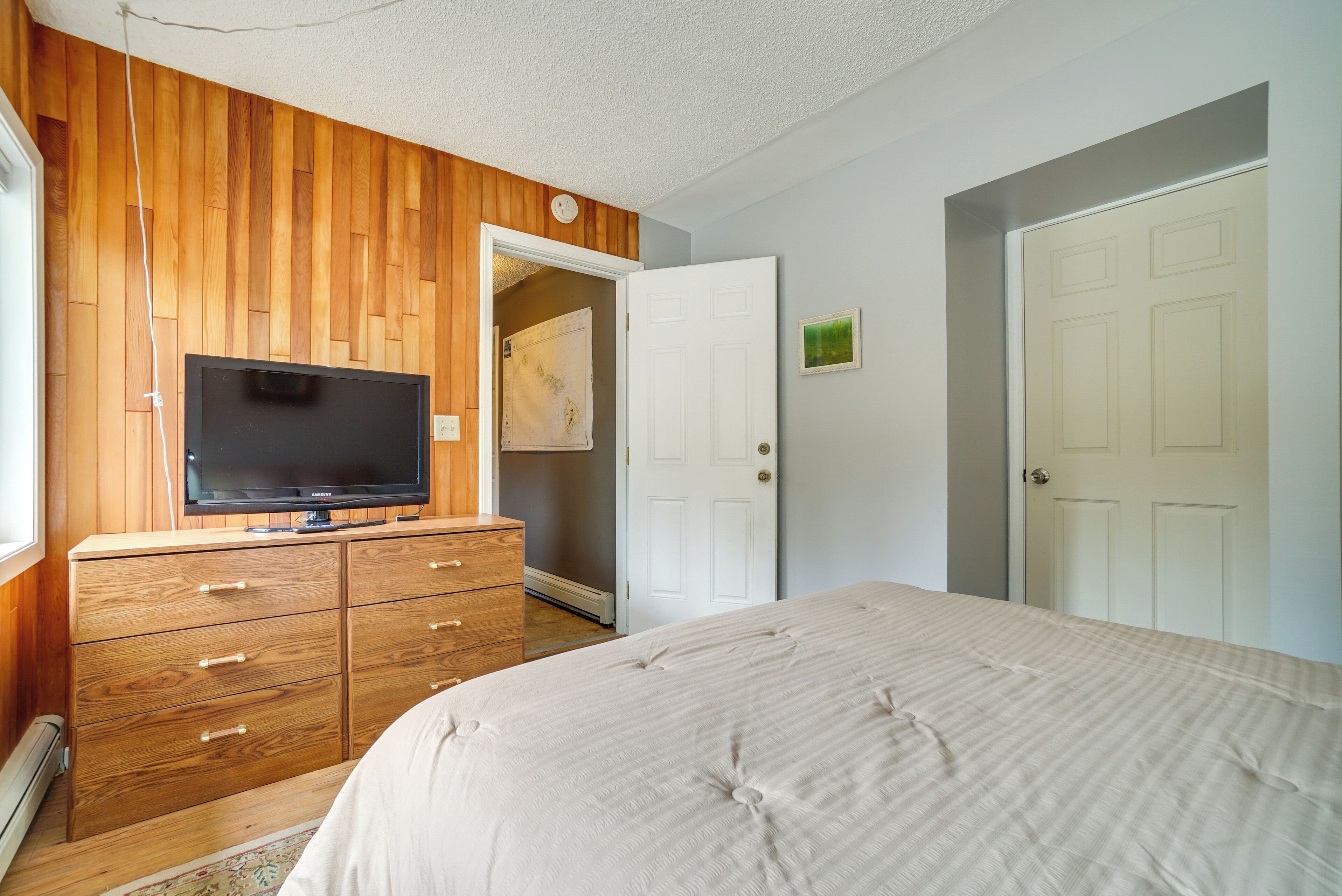 Una camera da letto con un comò in legno, una televisione, un letto e una porta bianca.