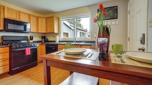 Una cocina con armarios de madera, estufa, microondas, ventana y una mesa de comedor con un florero.