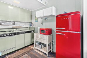 A retro kitchen with a red Galanz refrigerator, a vintage stove, and a white cabinet with a life-themed sign. - Beachy Studio Condo with Pool and steps from the OC Boardwalk (Ocean City)