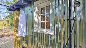 A rustic cabin with a wooden deck, a window with a white towel hanging, and a shower setup. - Hot Springs Studio ~ 3 Mi to National Park! (Hot Springs)