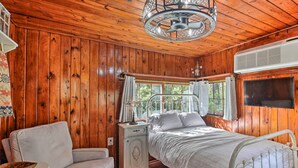 A wooden-paneled bedroom with a bed, a nightstand, a chair, and a window with curtains. - Hot Springs Studio ~ 3 Mi to National Park! (Hot Springs)