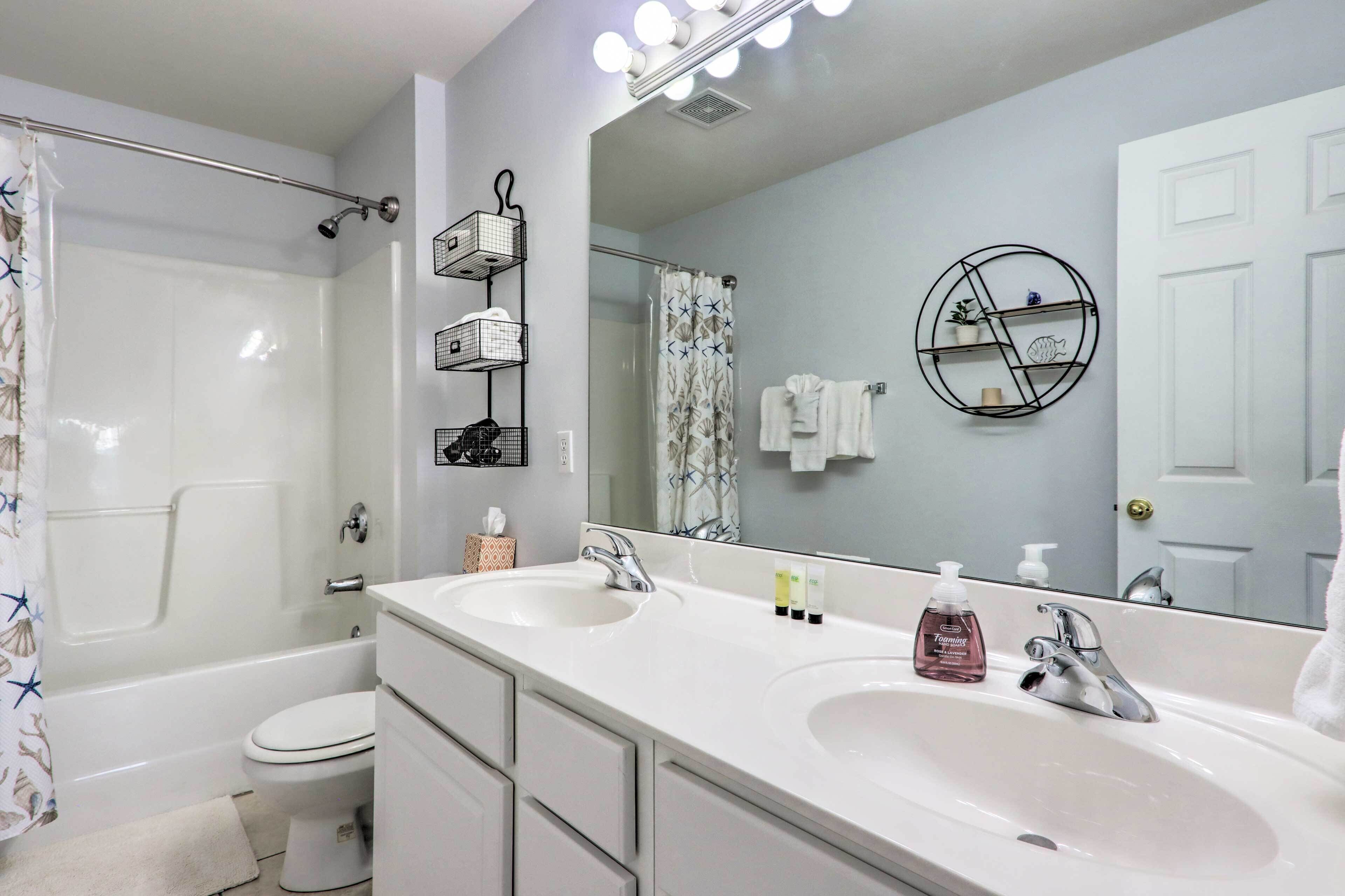 A bathroom with a double sink, a bathtub, a toilet, a shower curtain, and a mirror with lights.