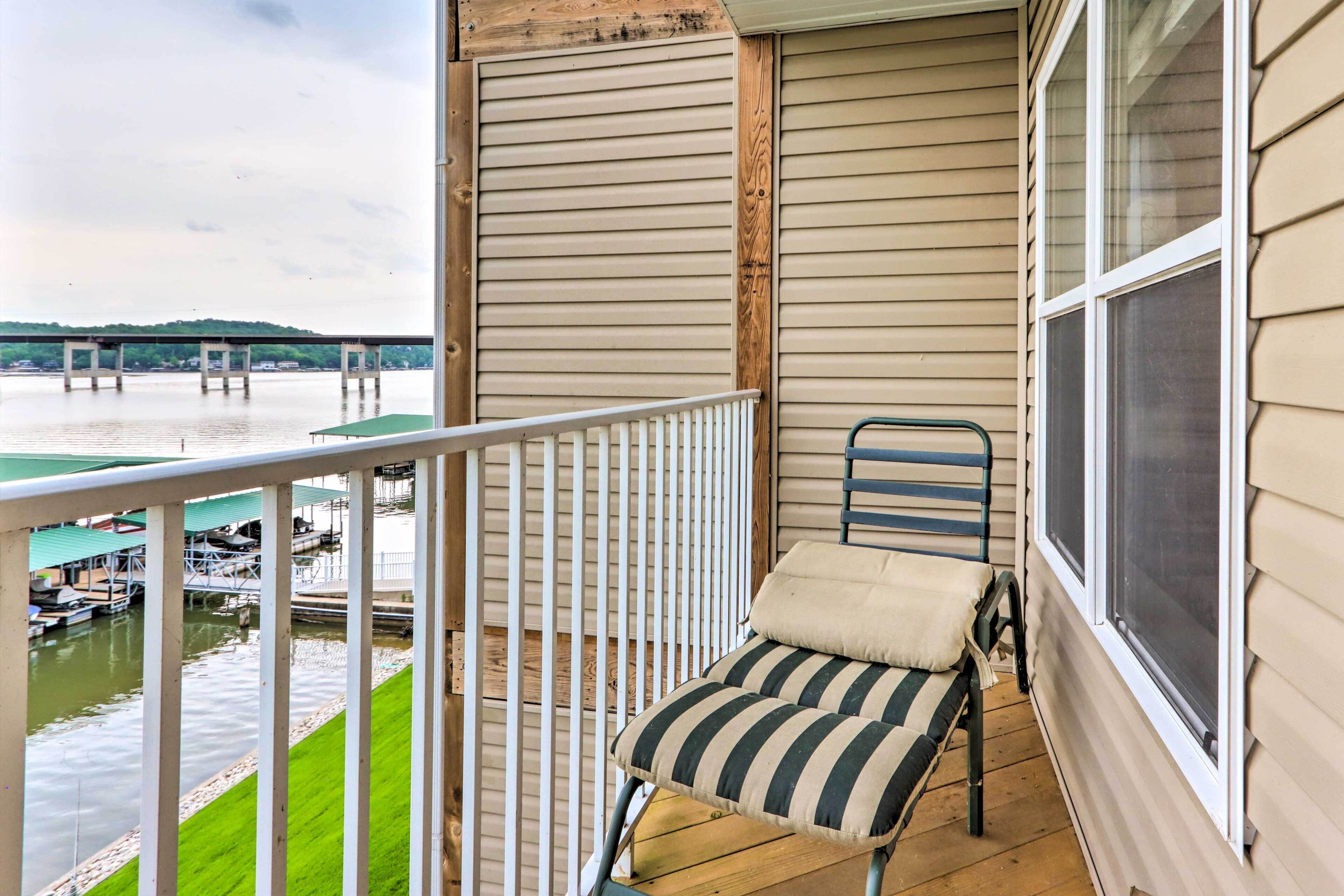 A balcony with a view of a river, a chair, and a small table.