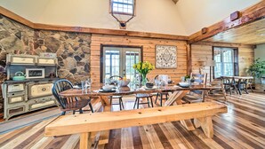 A rustic dining area with a long wooden table, stone wall, and wooden ceiling.