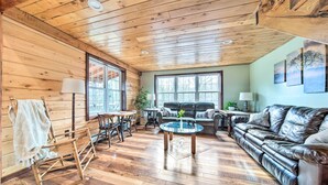 A cozy cabin interior with wooden walls, a leather sofa, a rocking chair, and a dining table.