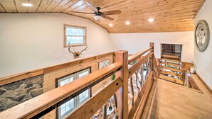 A wooden staircase with a railing, a ceiling fan, and a stone wall.