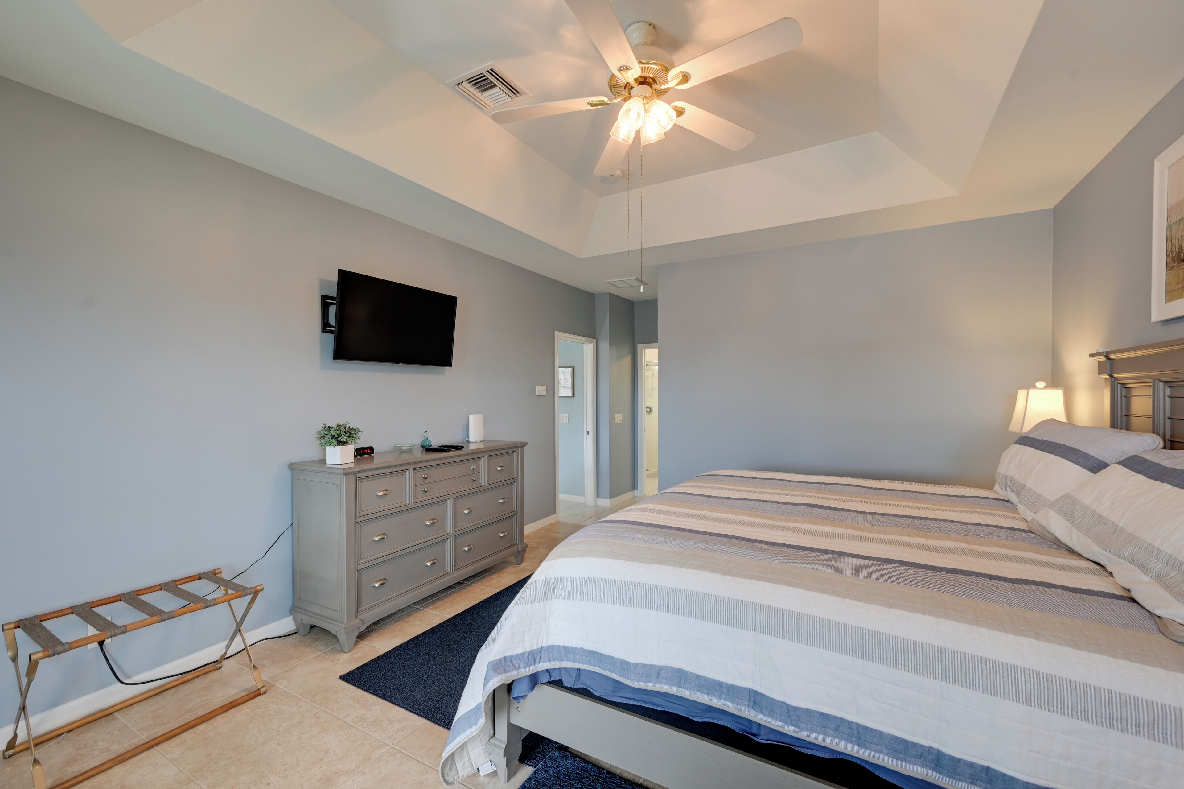 A bedroom with a bed, a dresser, a television, and a ceiling fan.