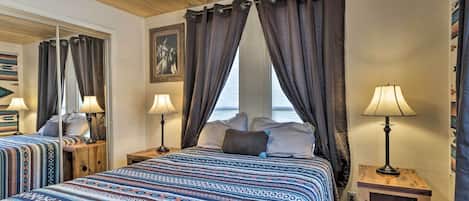 A bedroom with a large bed, two bedside tables with lamps, a ceiling fan, and a view of the sea through curtains.