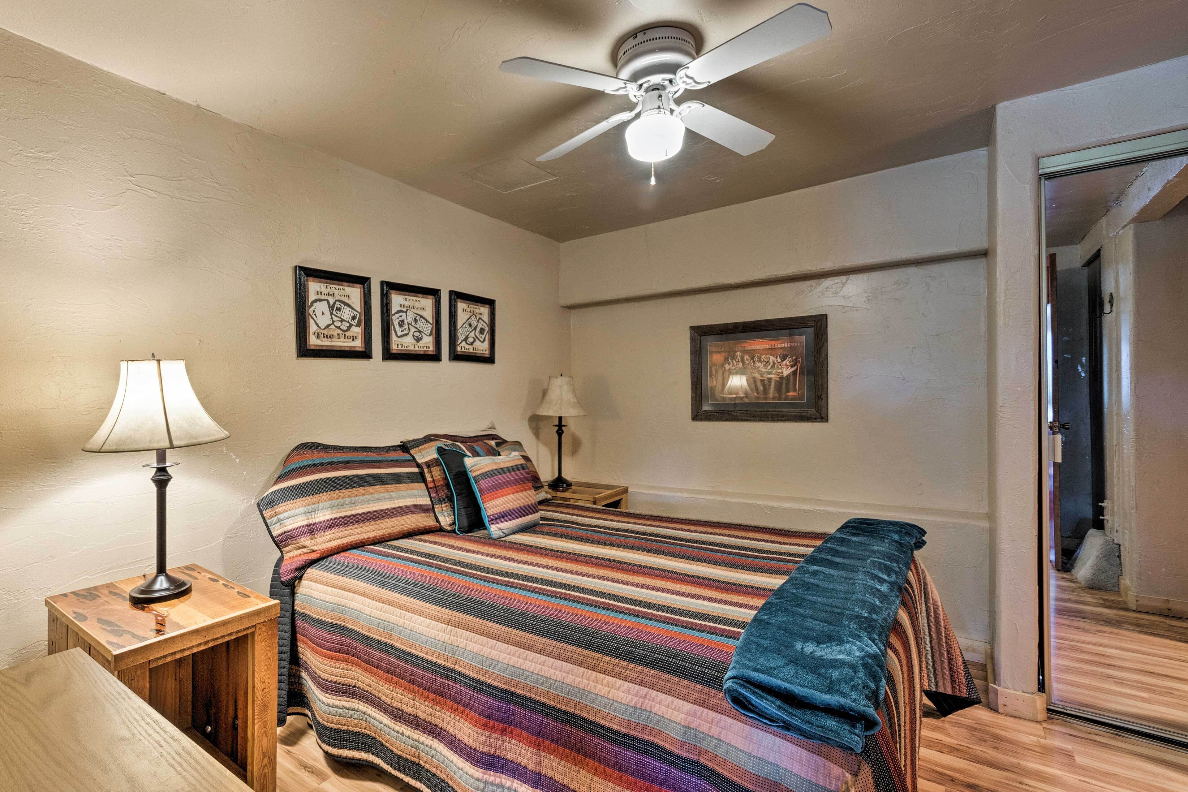 A bedroom with a bed, a ceiling fan, a nightstand with a lamp, and framed pictures on the wall.