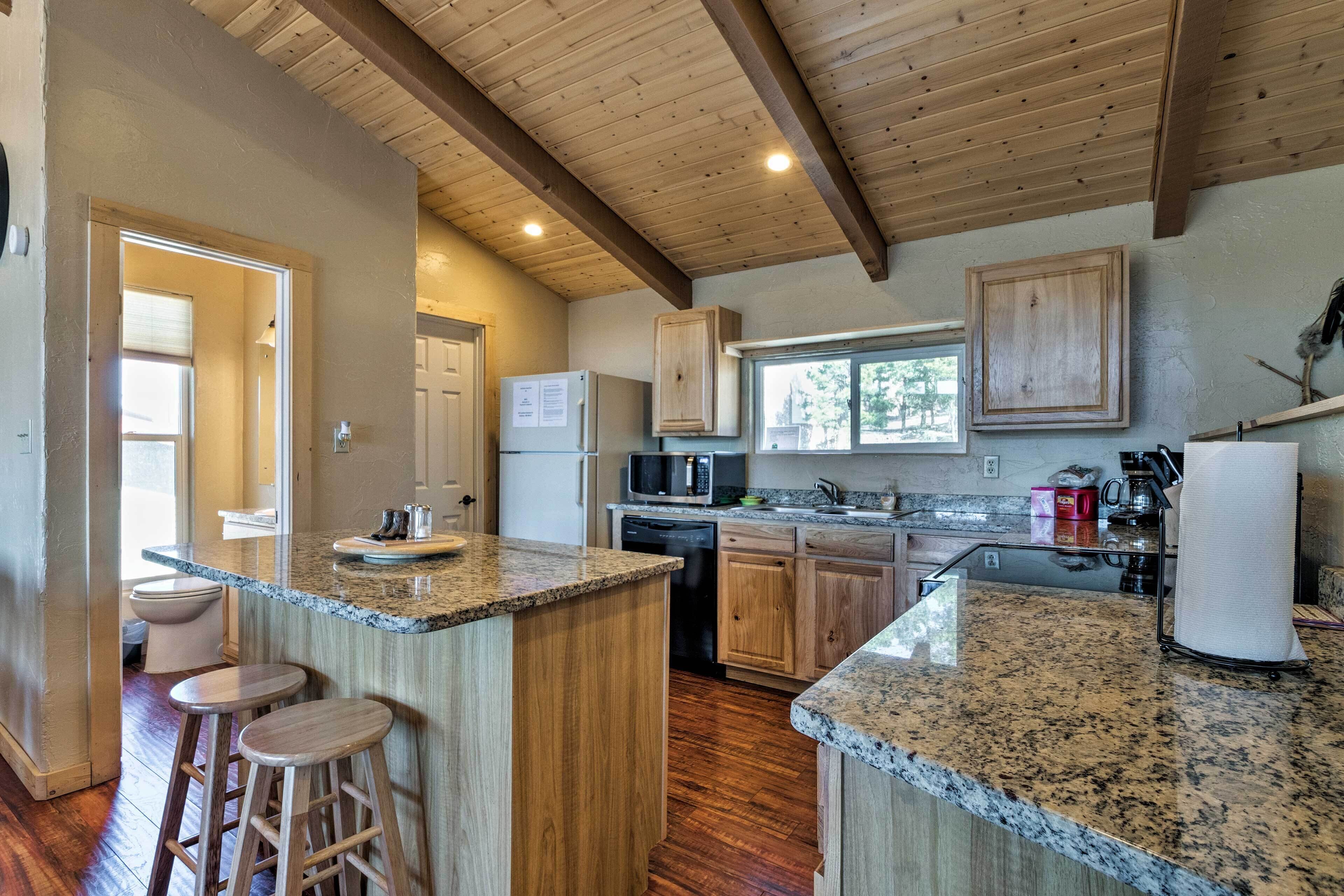 A kitchen with wooden cabinets, granite countertops, and a built-in island with stools.