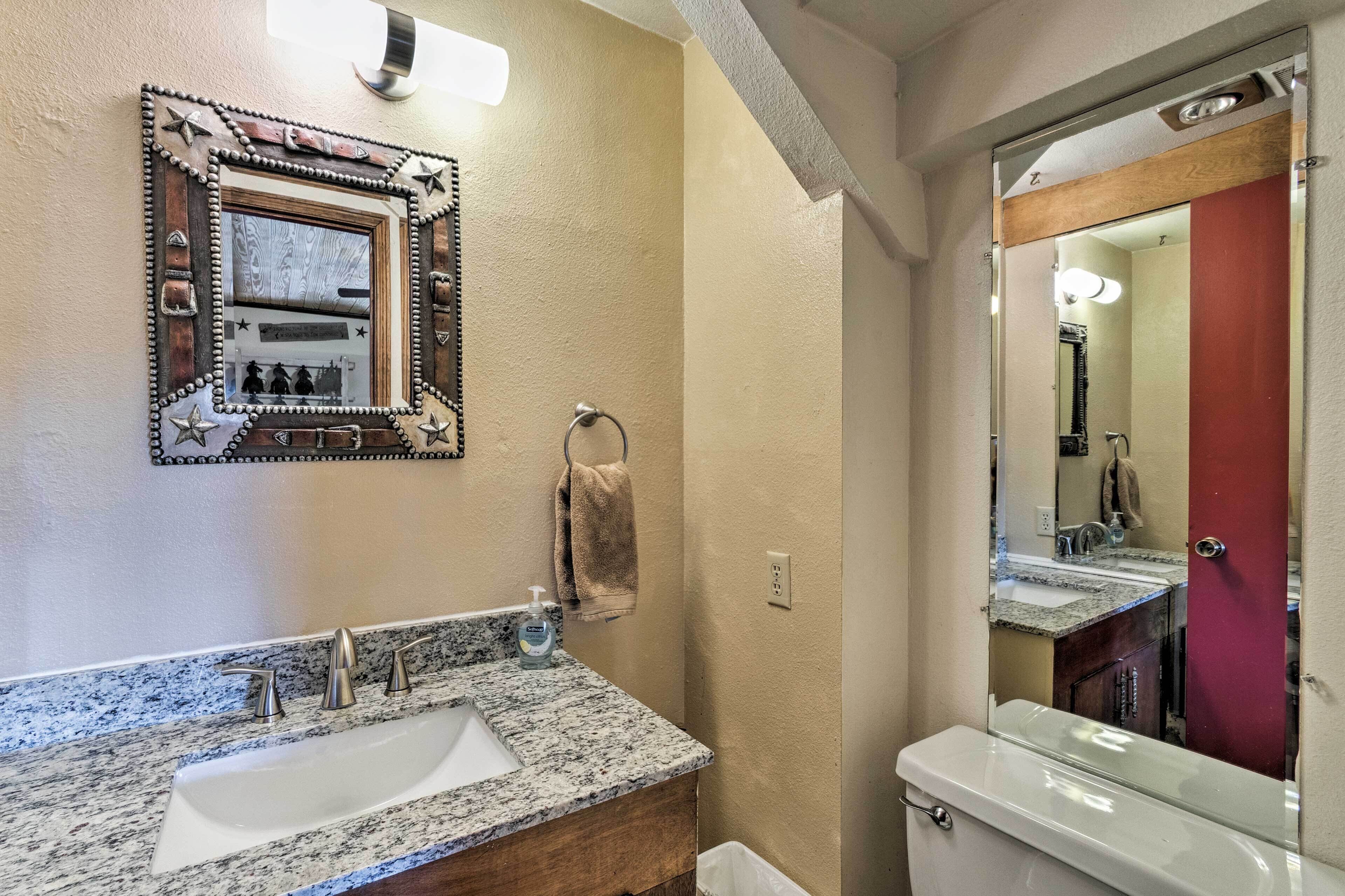 A bathroom with a granite countertop sink, a mirror with decorative frame, and a toilet.