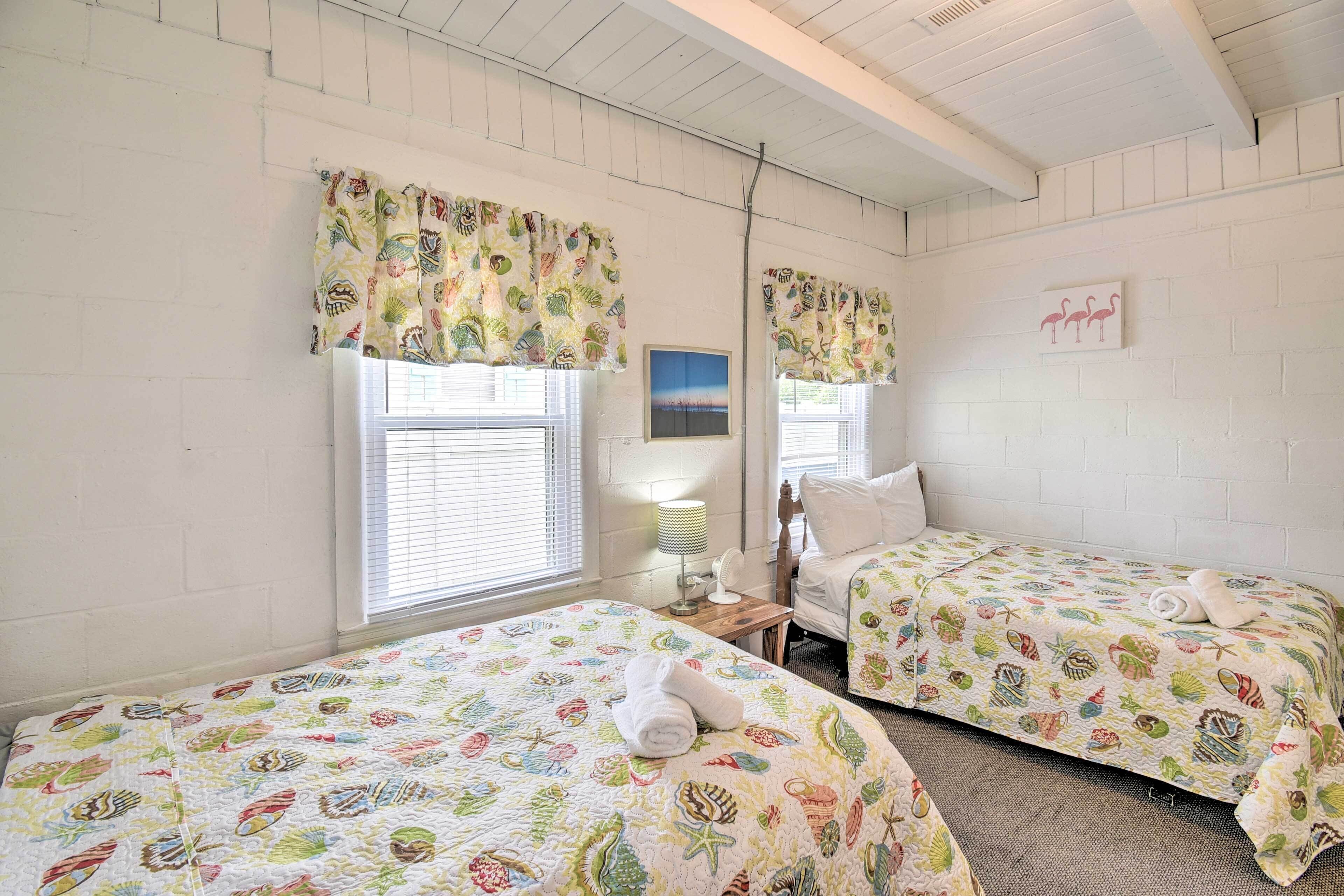 Een kamer met twee bedden, elk voorzien van een kleurrijk bedovertrek met vissen en zeedieren. Twee ramen met gordijnen, een klein tafeltje met een lamp en een schilderij aan de muur.