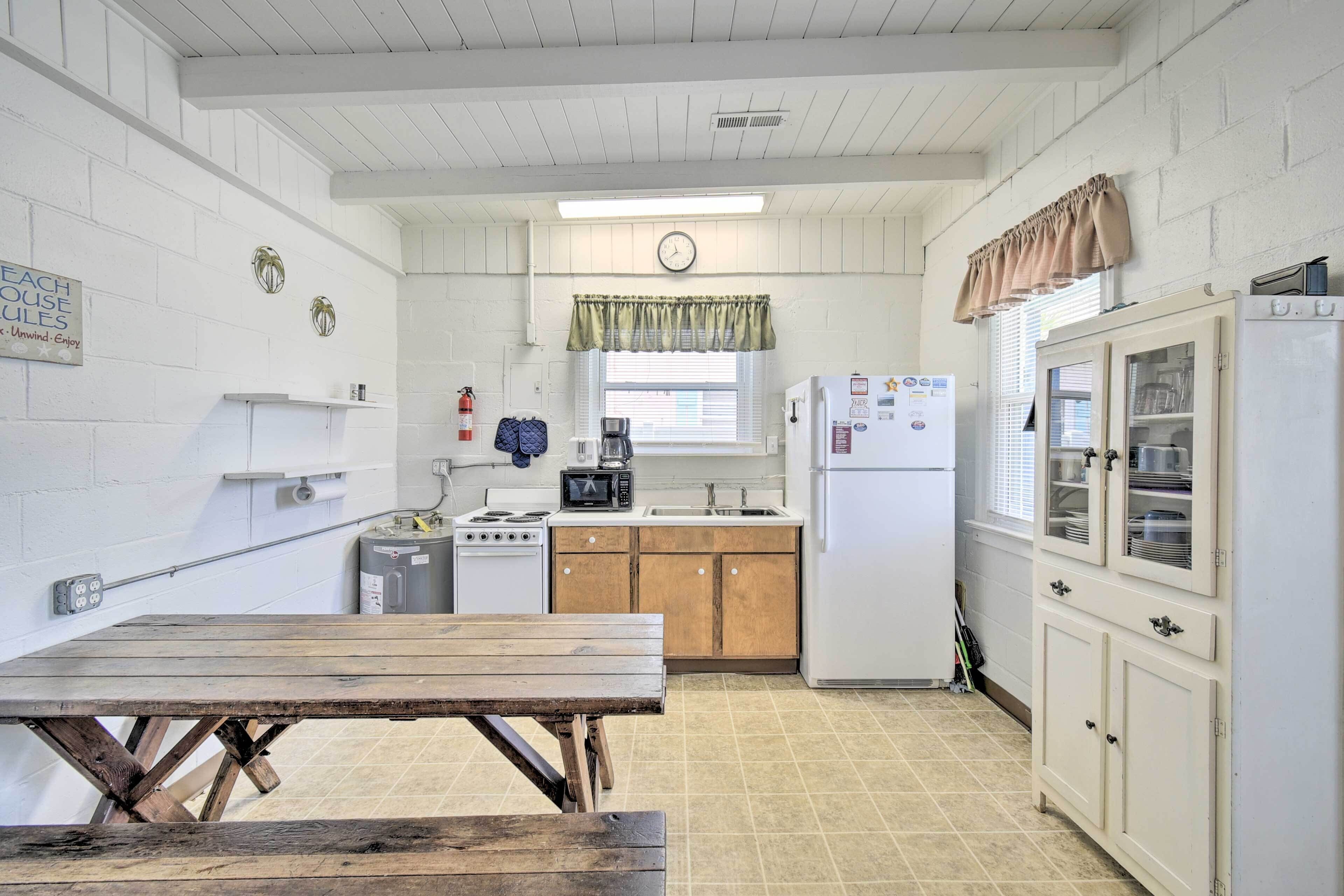 Una cocina funcional con una mesa de madera, armarios blancos, un refrigerador y un reloj en la pared.