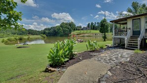 A lakeside property with a stone pathway leading to a wooden deck, surrounded by lush greenery and a clear view of the lake. - Game Room & Views: Lakefront Shelby Home! (Shelby)