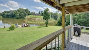 A wooden deck with a view of a lake, a grassy area, and a distant house. - Game Room & Views: Lakefront Shelby Home! (Shelby)