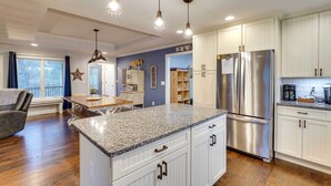 Una cocina moderna con armarios blancos, un refrigerador de acero inoxidable, encimeras de granito e iluminación colgante.