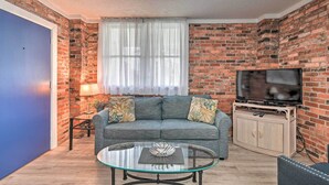 A living room with a brick wall, a blue door, a grey sofa, a glass coffee table, and a TV stand. - Ground Floor Unit: 10 Miles to Myrtle Beach (Murrells Inlet)