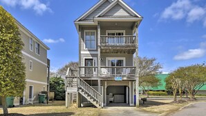 A two-story building with a balcony on the upper floor, a covered front porch, and a garage entrance. - Home w/ Deck in Corolla Light: Walk to Beach! (Corolla)