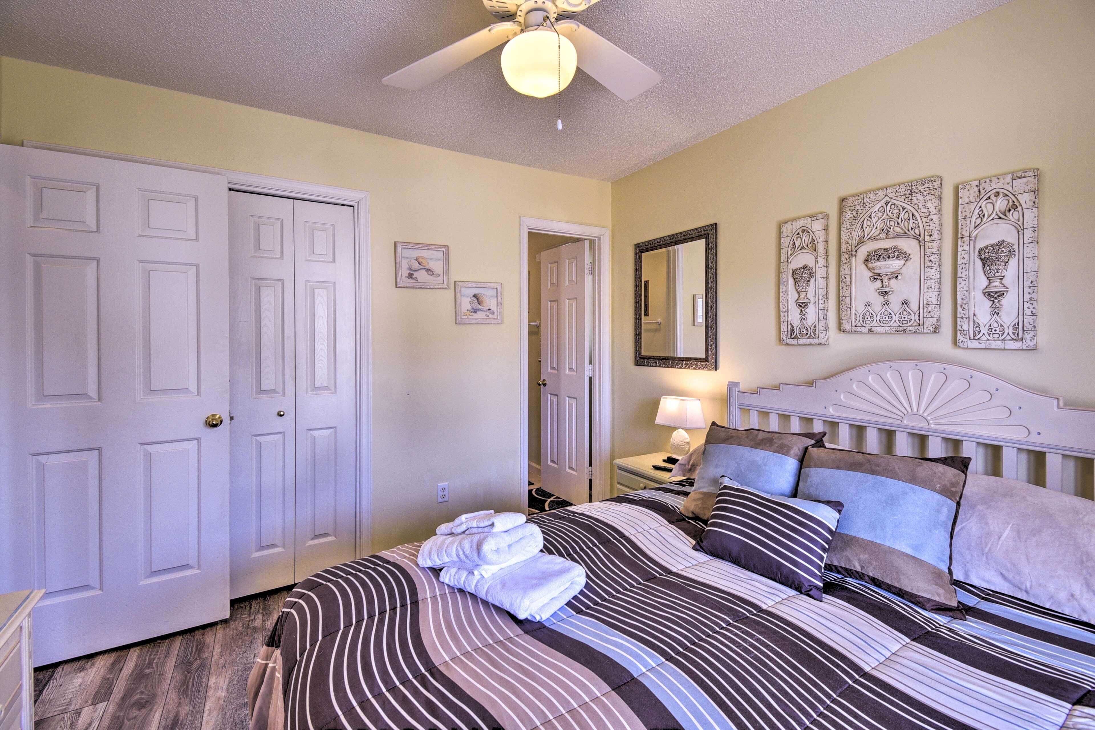 A bedroom with a bed, a nightstand, a lamp, a ceiling fan, and a door.