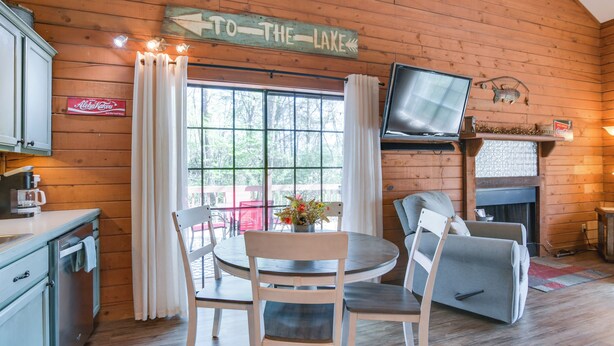 Ein Holzblockhaus-Interieur mit Esstisch, Stühlen, einem Fernseher und einem Schild mit der Aufschrift 'ZUM SEE'.