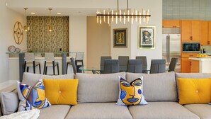 Ein modernes Wohnzimmer mit Sofa, Essbereich mit Stühlen, Küche mit Schränken und einer Pendelleuchte.