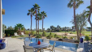 Ein Poolbereich mit Tisch und Stühlen, umgeben von Palmen und Blick auf einen Golfplatz.