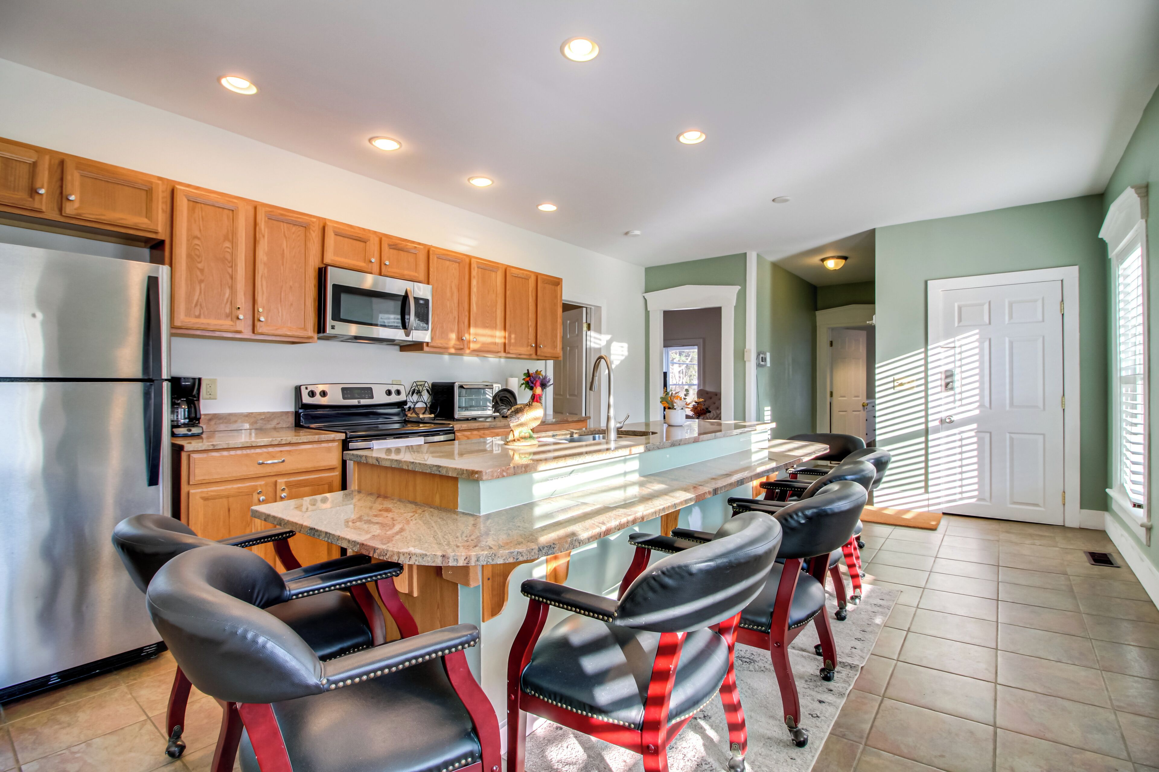 A modern kitchen with wooden cabinets, stainless steel appliances, a large island with bar stools, and a view to the living area.