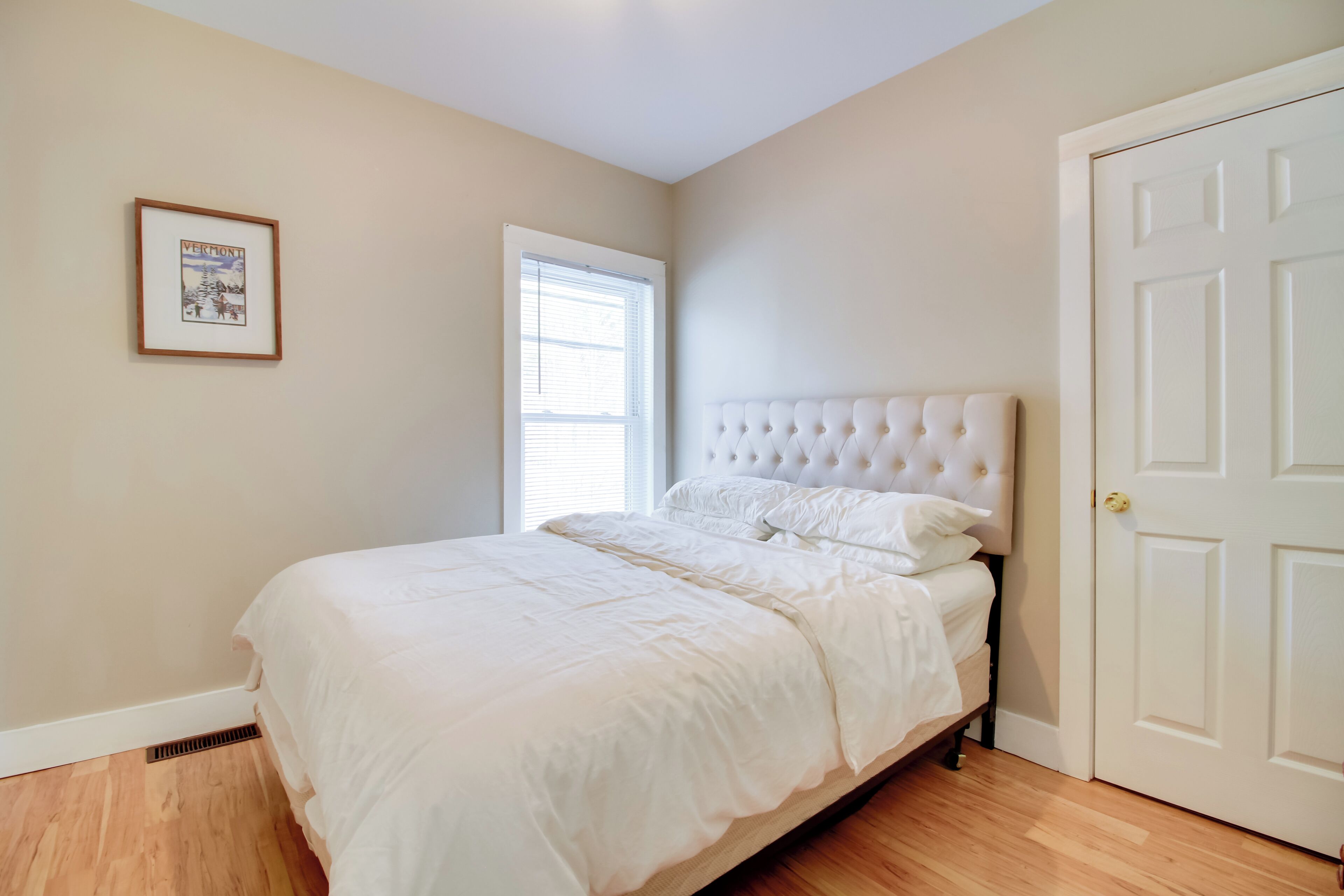 A bedroom with a white bed, a framed picture on the wall, and a door.