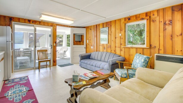 A cozy living room with wooden walls, a grey sofa, a beige sofa, and a blue patterned chair. - Lake Stinson Cottage w/ Sunroom & Shared Dock! (Rumney)