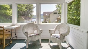 A room with two wicker chairs and a wooden table, large windows with a view of a lake and buildings. - Lake Stinson Cottage w/ Sunroom & Shared Dock! (Rumney)