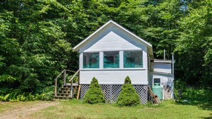 A small, single-story house with a white exterior and a fenced yard. - Lake Stinson Cottage w/ Sunroom & Shared Dock! (Rumney)