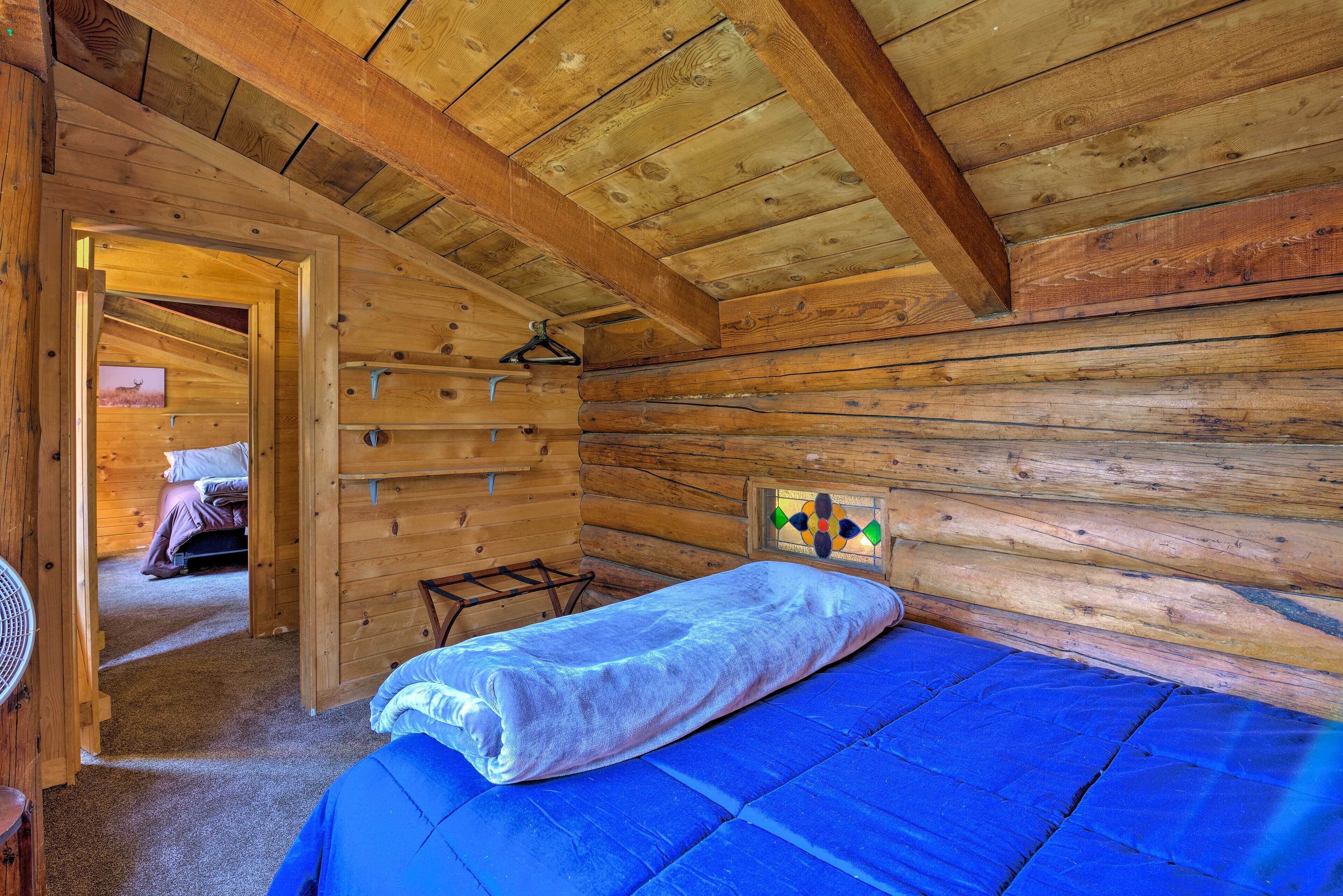 Una habitación tipo cabaña de madera con una cama, una lámpara colgante y una puerta que da a otra habitación.