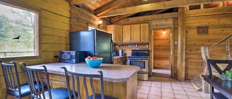 Une cuisine rustique aménagée dans une cabane en bois, avec un îlot central, des tabourets de bar, un réfrigérateur, un four à micro-ondes et une cuisinière.