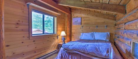 A cozy cabin room with a bed, a window, and a picture on the wall.