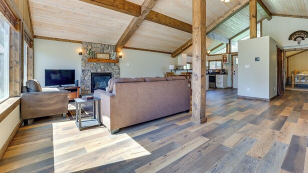 A spacious living area with a stone fireplace, wooden beams, and a large sofa. - Donnelly Cabin w/ Fire Pit: 5 Mi to Boat & Ski! (Donnelly)