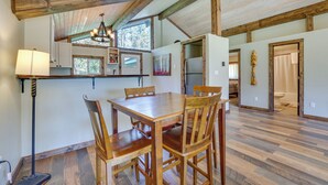 A spacious dining area with a wooden table and chairs, a chandelier, and a view of the kitchen and bathroom. - Donnelly Cabin w/ Fire Pit: 5 Mi to Boat & Ski! (Donnelly)