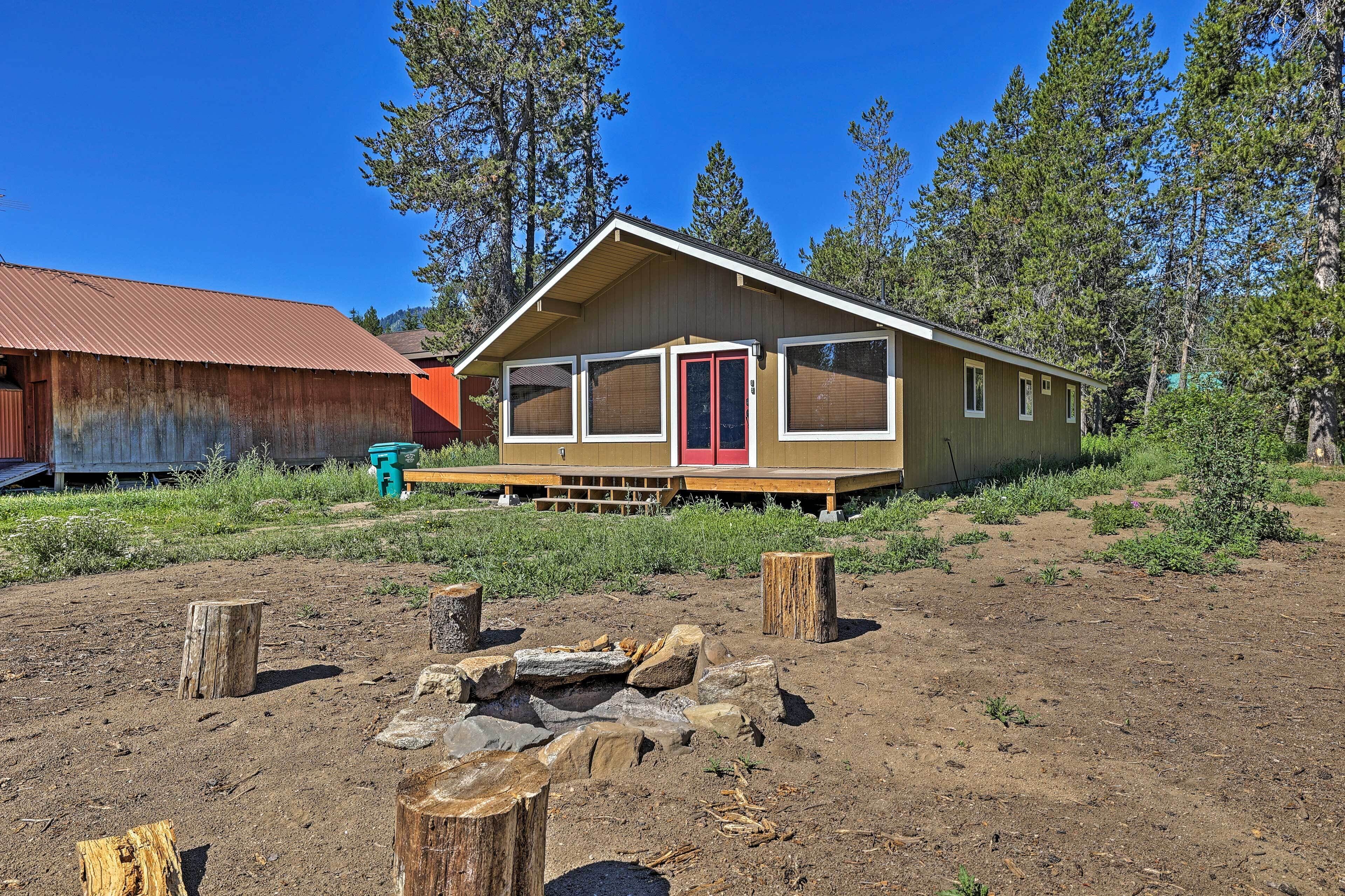 A cabin with a wooden deck, large windows, and a red door.